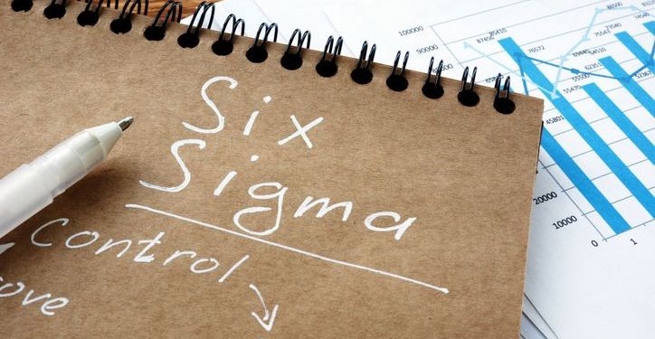 Six Sigma written on a notebook with process improvement charts in background